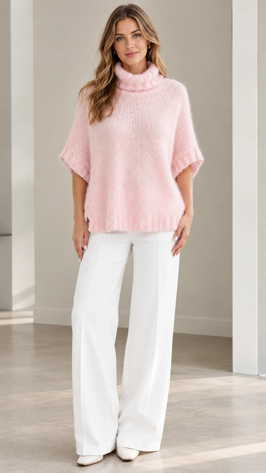 Front view of model wearing Light Pink short sleeve fuzzy turtleneck poncho sweater with white wide-leg trousers