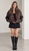 Front view of model wearing dark brown faux leather bomber jacket with plush fur collar