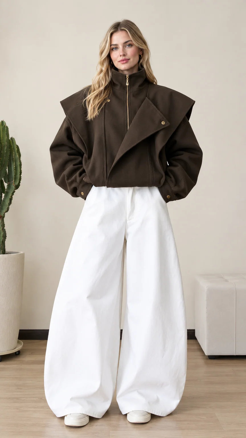 Front full view of woman wearing dark brown asymmetrical flap zip-up jacket with wide white trousers