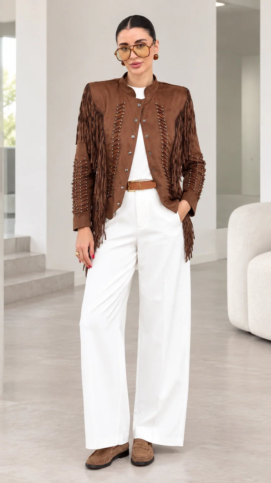Front full-length view of model wearing brown faux suede fringe jacket with white trousers