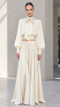 Front view of model wearing ivory satin bow tie blouse and matching pleated maxi skirt set