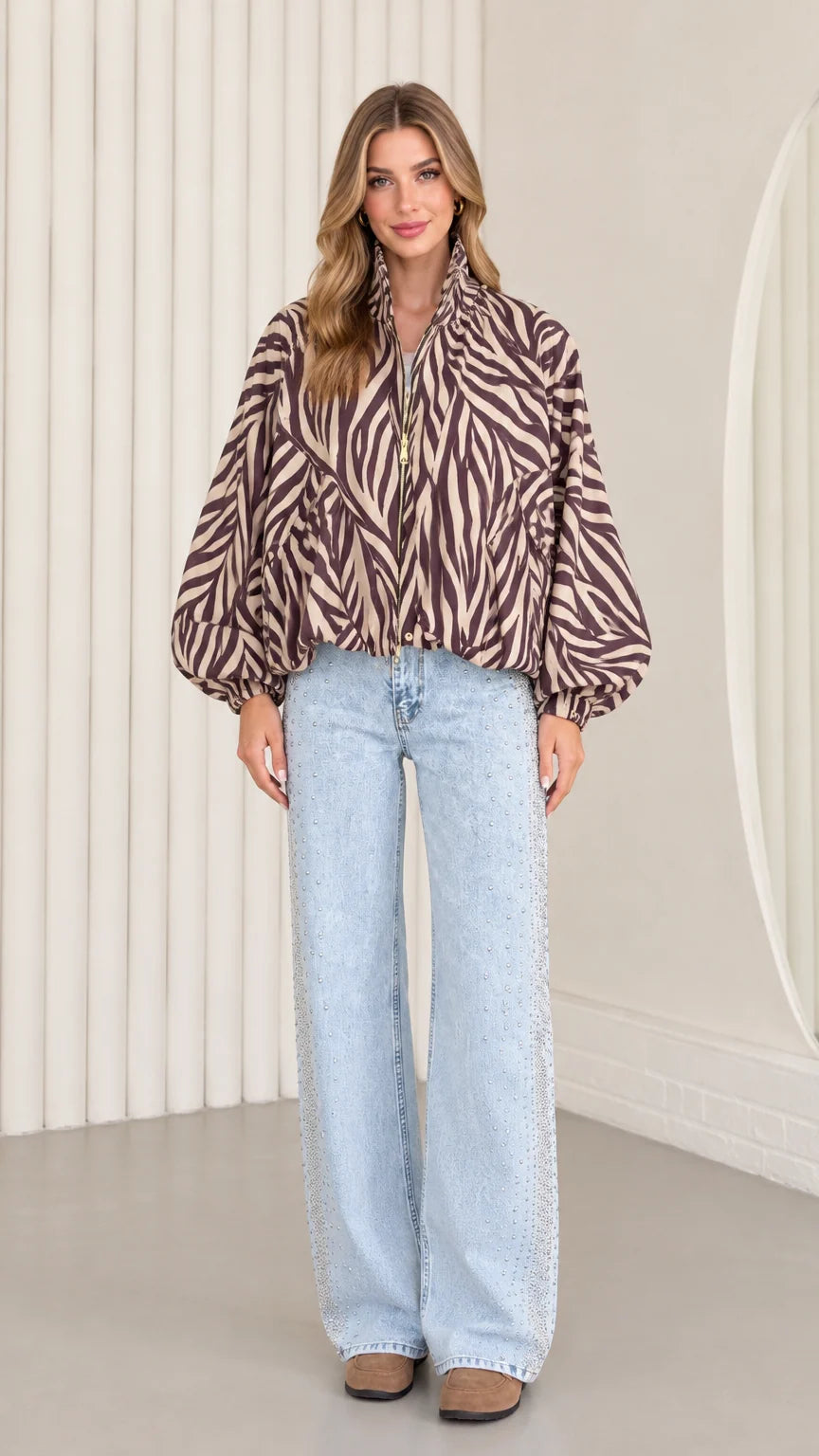 Front view of model wearing mocha brown zebra print balloon sleeve zip-up jacket with light-wash wide-leg jeans
