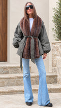 Woman wearing an olive green belted jacket with brown faux fur trim and flare jeans