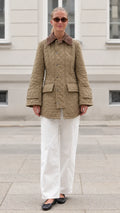 Front full-length view of woman wearing khaki diamond quilted barn jacket with white pants