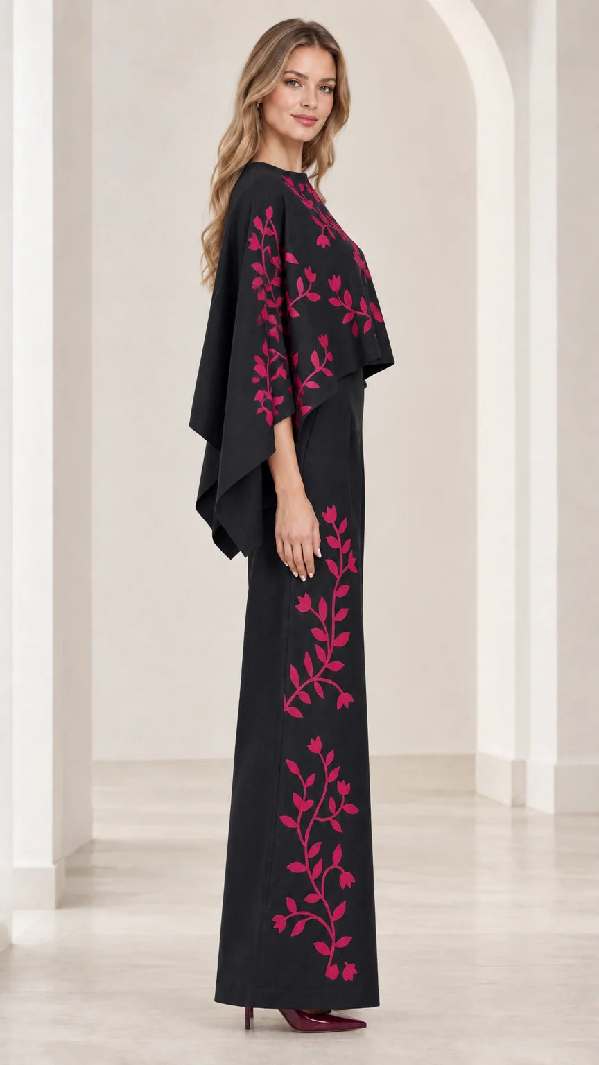 Side profile view of black embroidered cape jumpsuit showing draped capelet