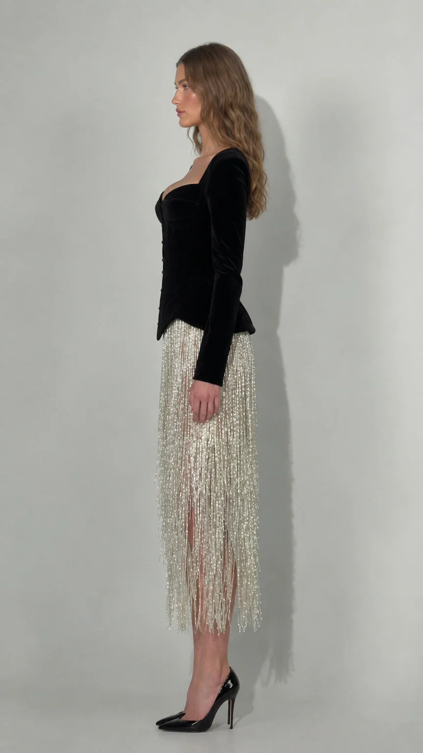 Side profile of black velvet corset midi dress with flowing fringe skirt