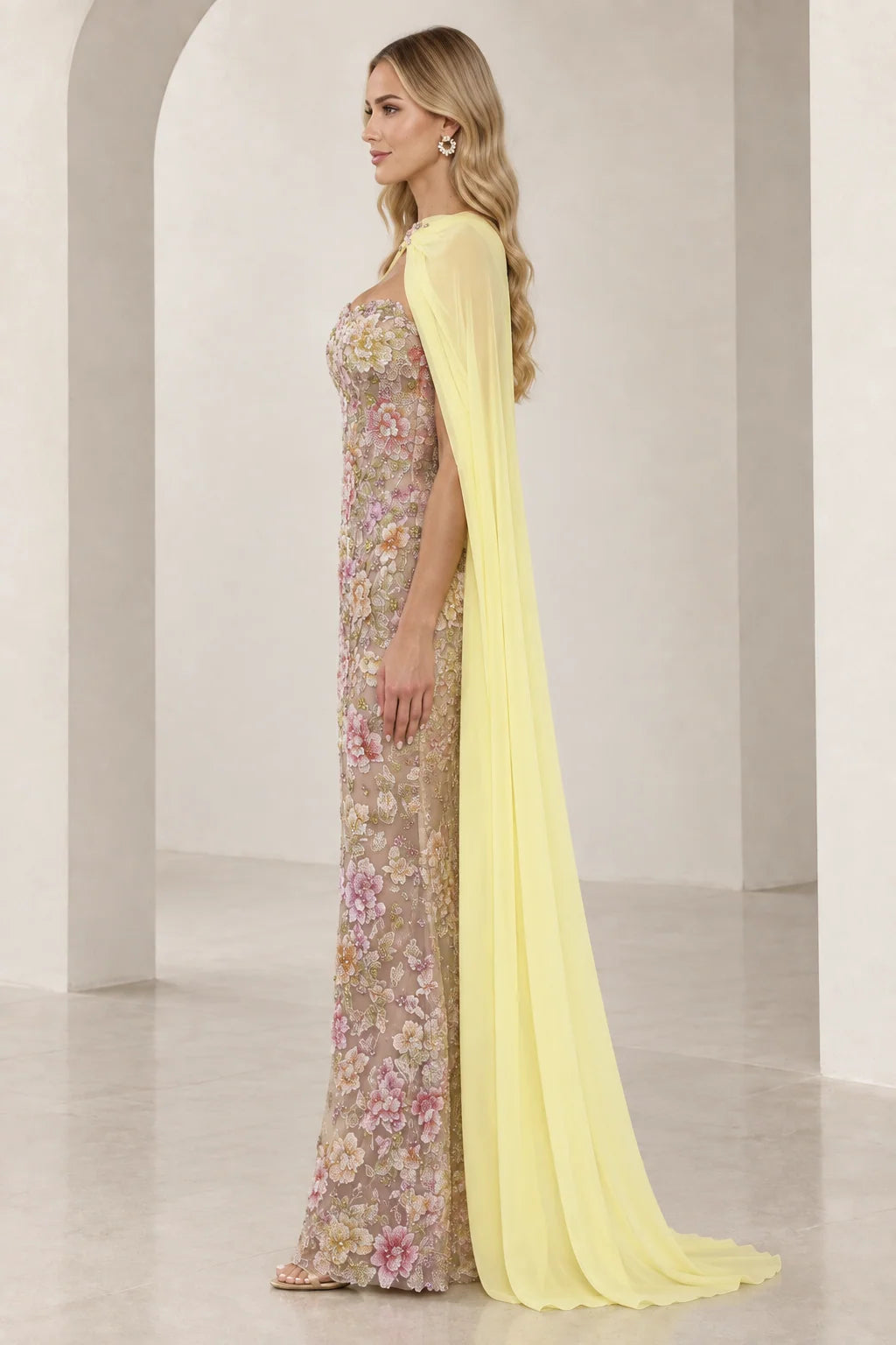 Side profile of model wearing floral embroidered column gown with flowing yellow chiffon cape