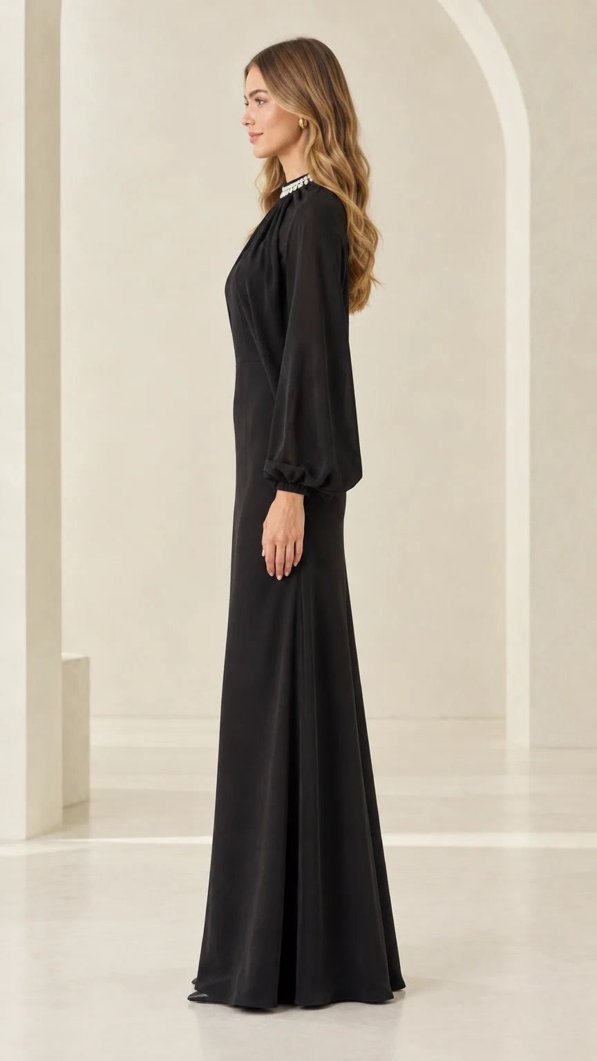 Side profile view of woman modeling black long sleeve cape formal gown