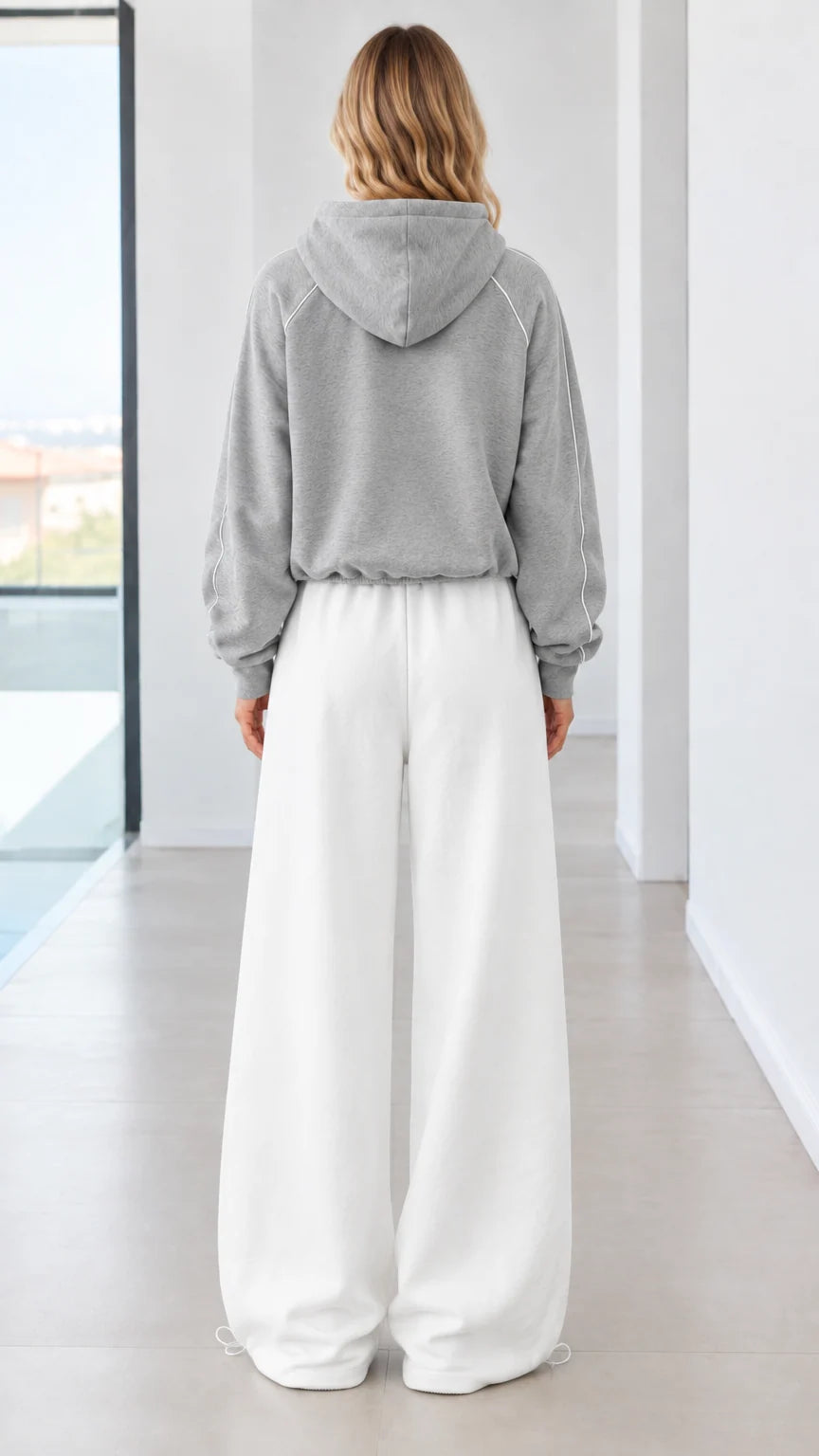 Back view of model wearing grey zip-up hoodie and white wide-leg sweatpants