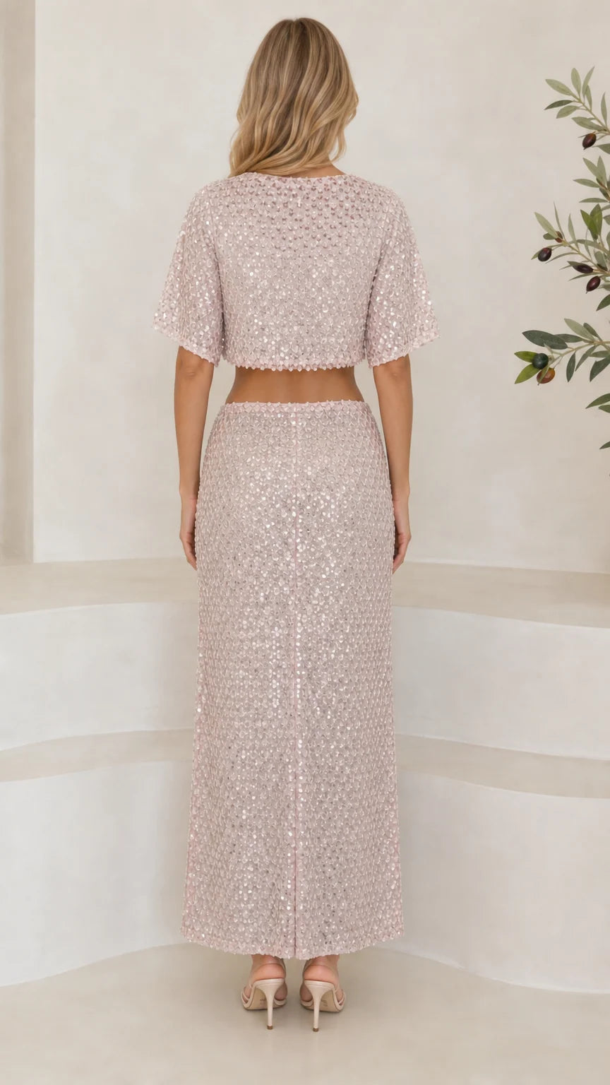 Back full-length view of woman in blush pink sequin crop top and column maxi skirt