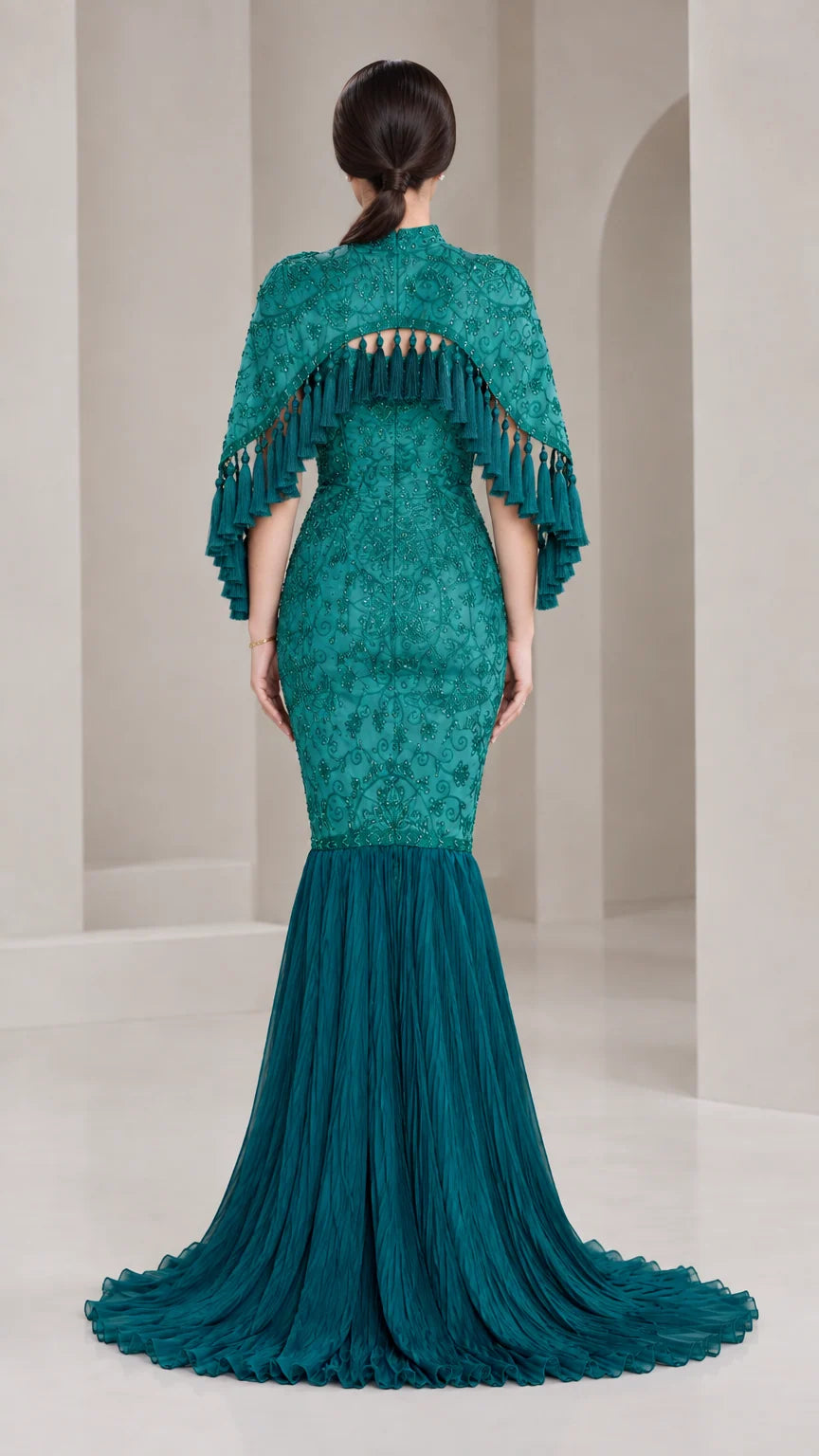 Back view of model showing Teal Green embroidered capelet and flowing pleated skirt