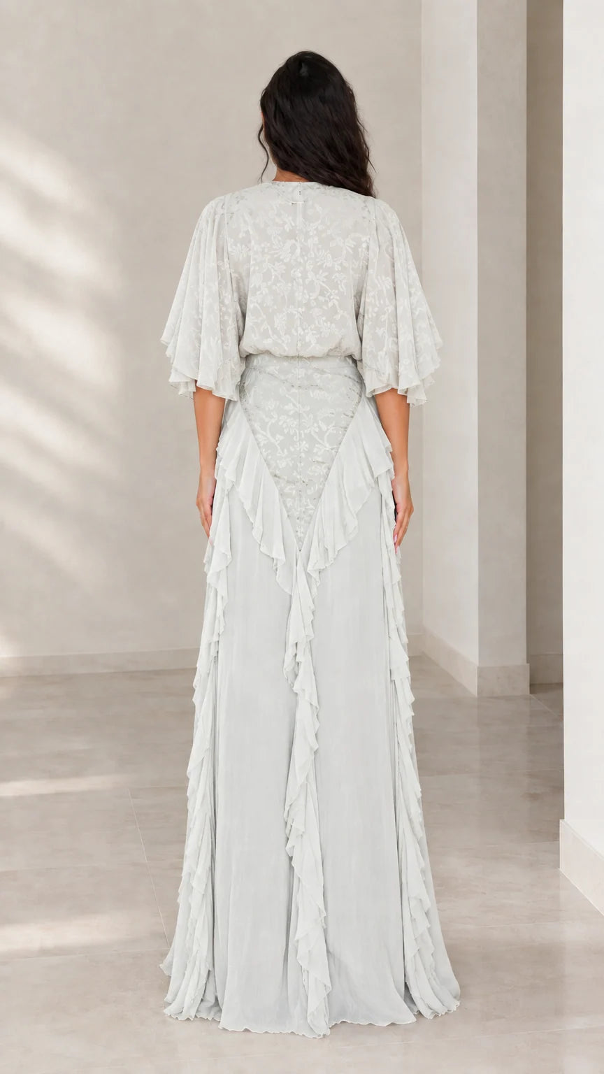 Back view of woman wearing ice blue flutter sleeve maxi gown with ruffle details