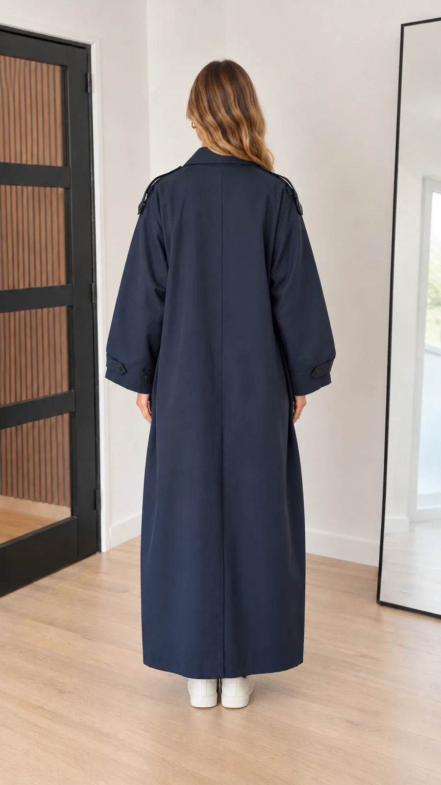 Back view of woman wearing navy blue full-length trench coat with back vent