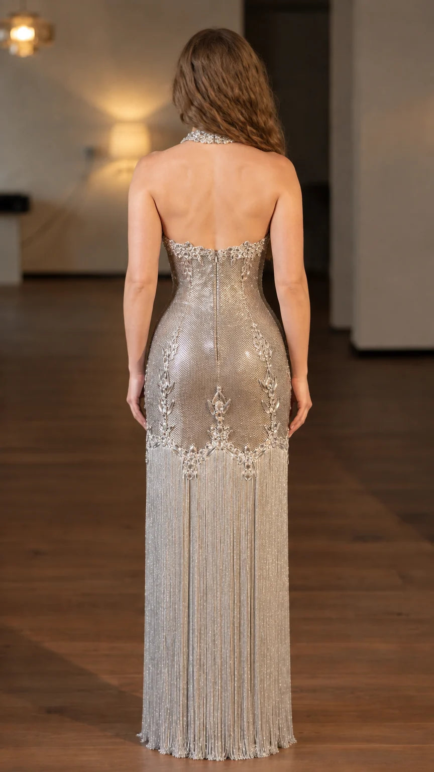 Back view of model showing open back silhouette of silver beaded fringe formal dress