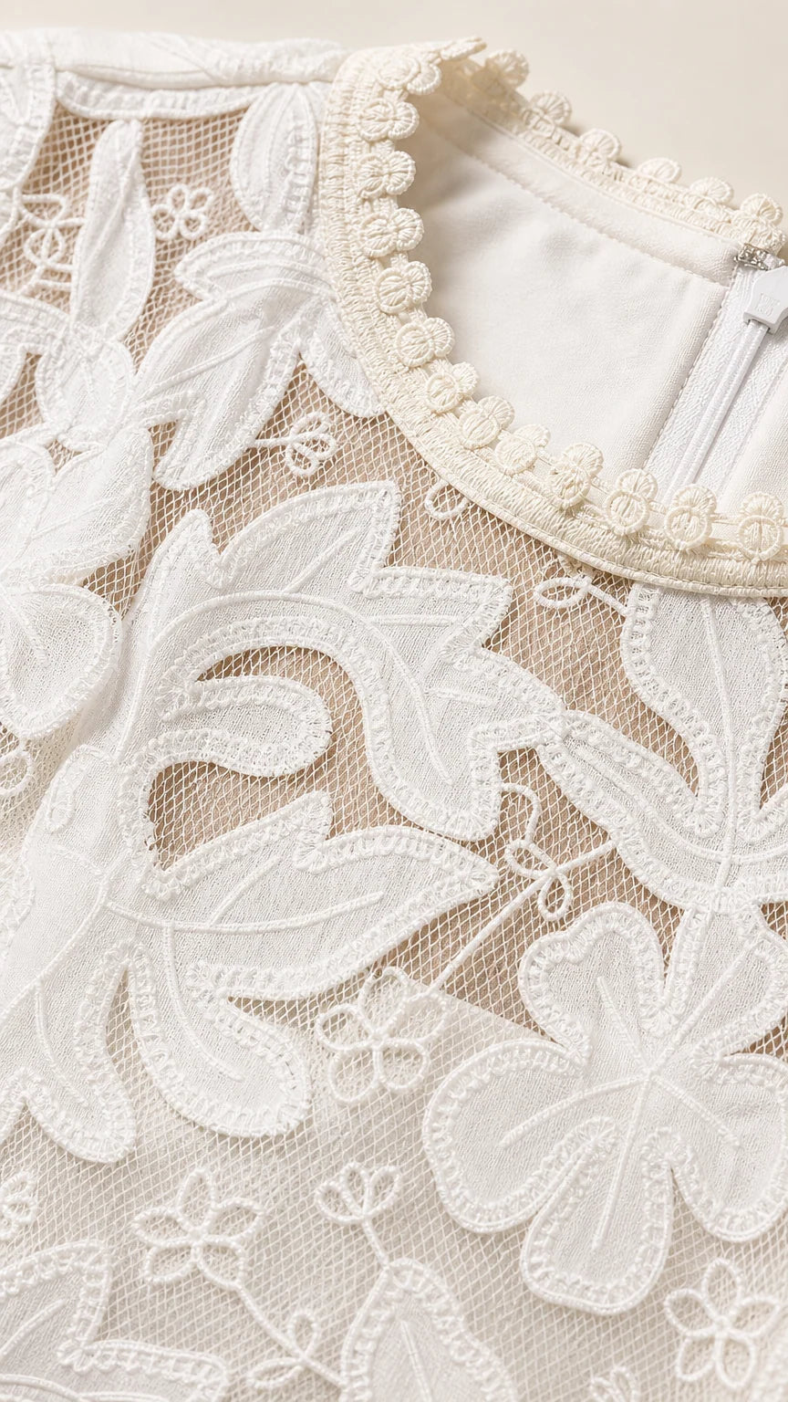 Close-up detail of white floral embroidery and beaded pearl-like trim along the neckline