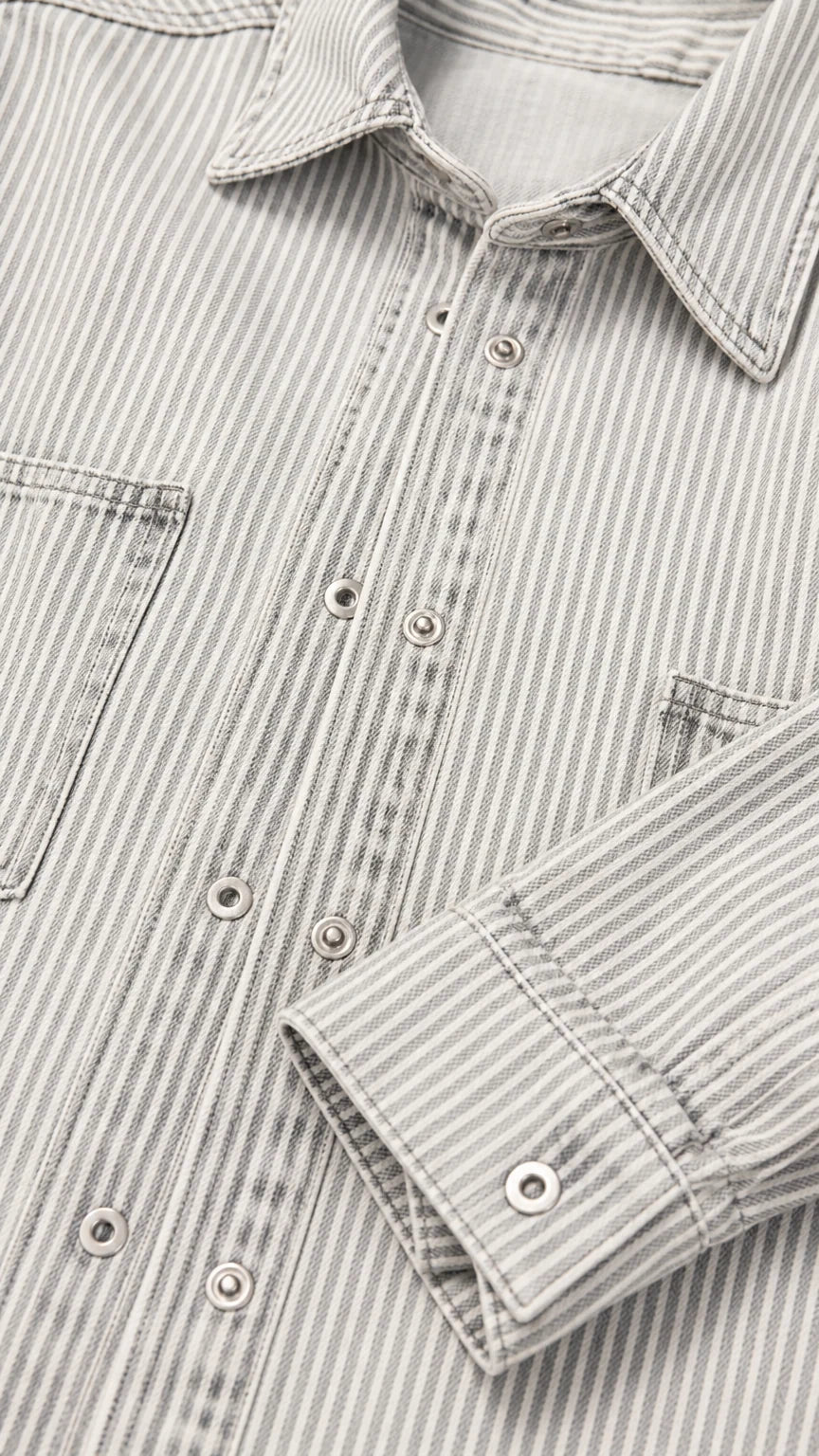 Close-up detail of striped denim fabric showing collar, snap buttons, and chest pocket