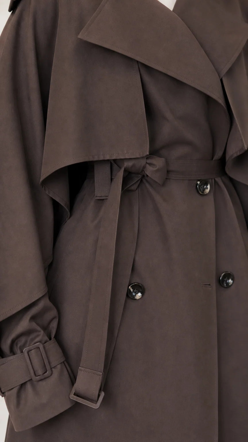 Close-up of dark brown trench coat cape overlay, belt buckle, cuff strap, and buttons