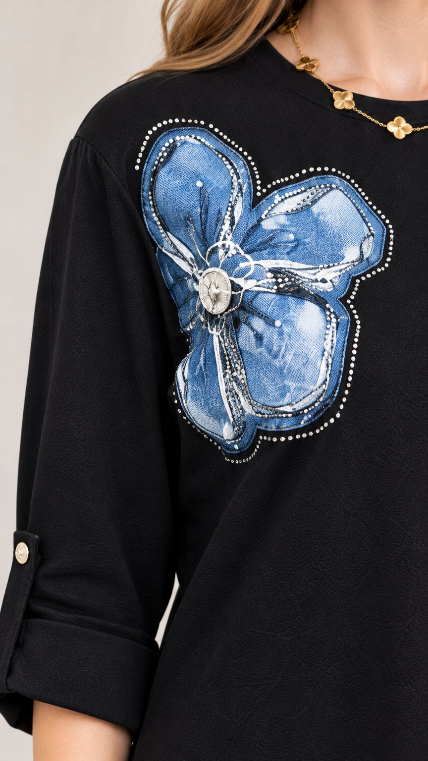 Close-up detail of embroidered blue floral appliqué and roll-tab sleeve cuff