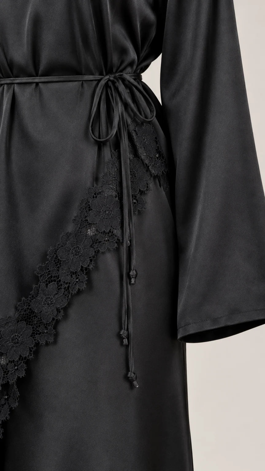 Close-up detail of lace trim, satin fabric, and waist tie cords on black dress