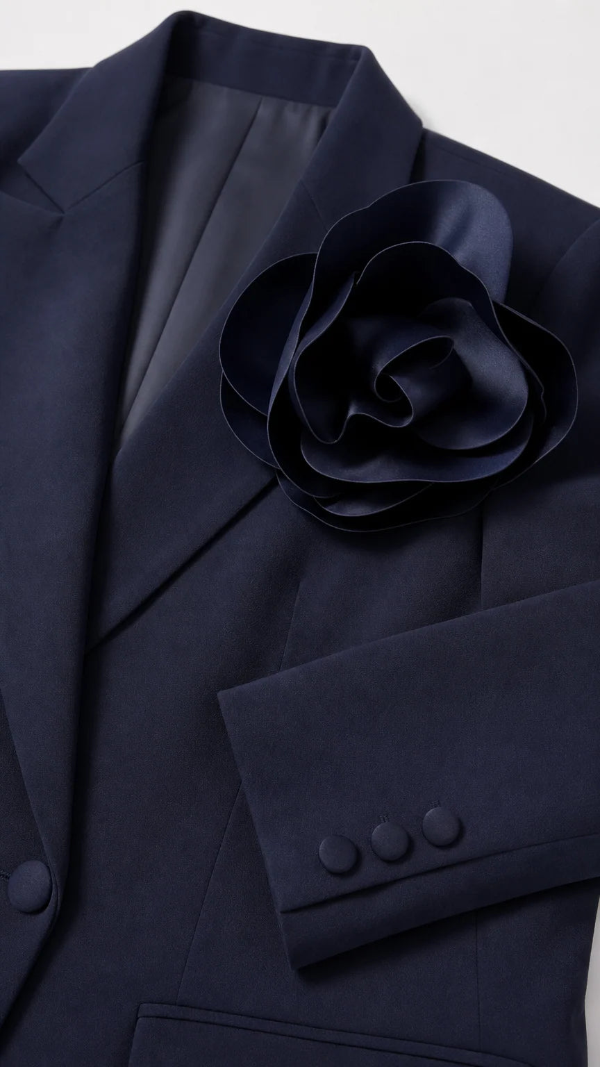 Close-up of the navy blazer lapel, sculptural flower detail, buttons, and sleeve