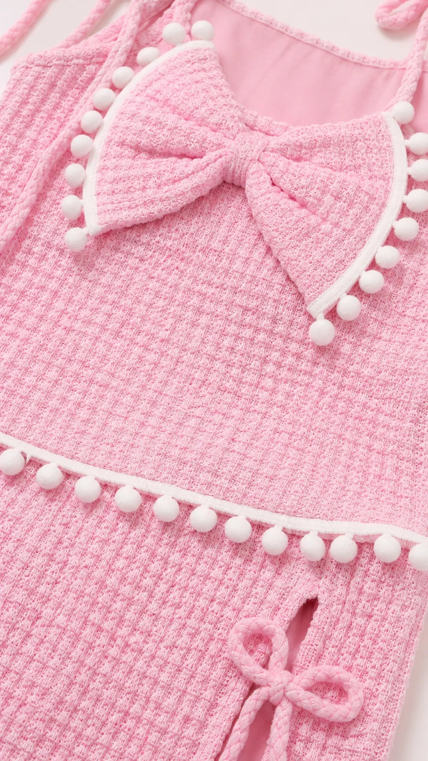 Close-up detail of pink textured knit fabric, bow accent, and white pompom trim