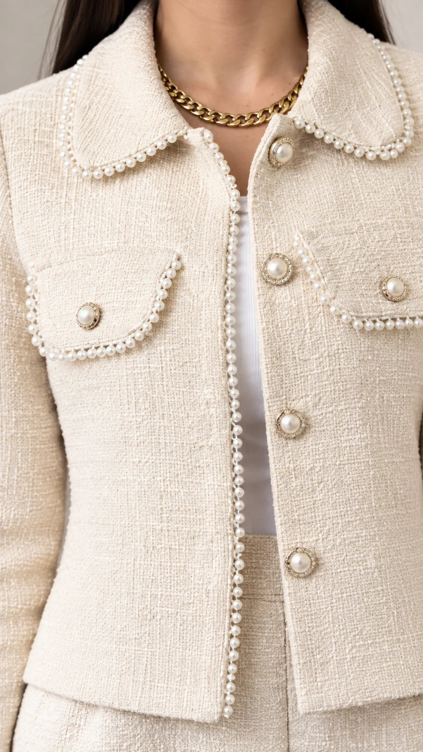 Close-up detail of cream tweed jacket highlighting pearl trim on the collar, pockets, and pearl buttons
