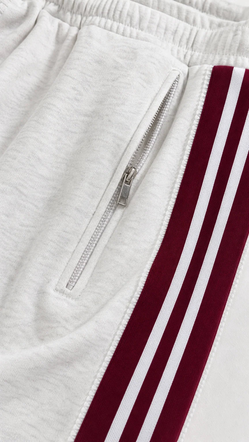 Close-up detail of white track pant zipper pocket and striped side trim