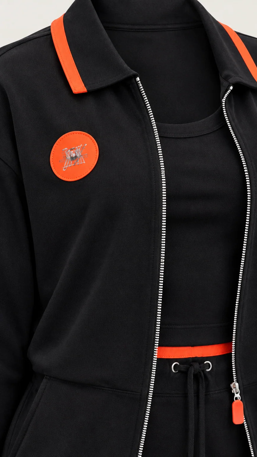 Close-up detail of black jacket collar, zipper, orange patch, and drawstring waist