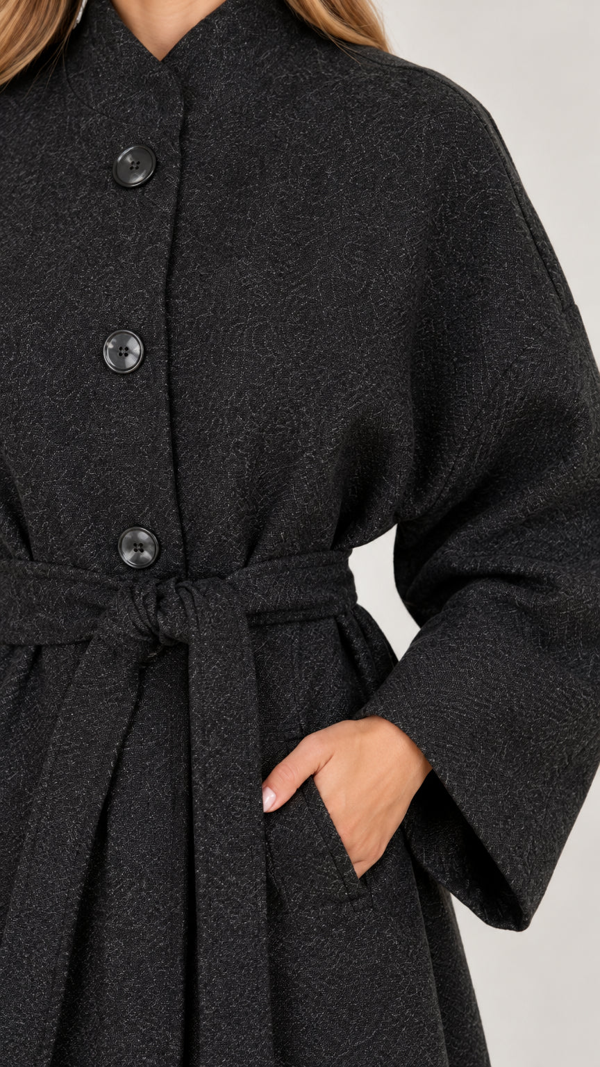 Close-up detail of charcoal grey bouclé textured coat showing stand collar, buttons, belt, and pocket