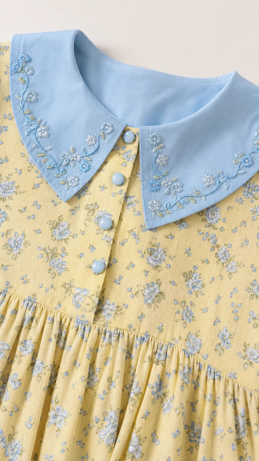 Close-up of contrast light blue embroidered Peter Pan collar with decorative buttons and yellow floral pattern